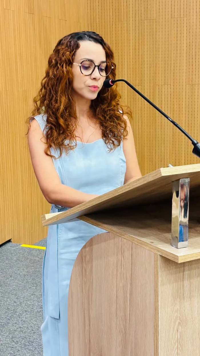 Edna Costa sentada em cadeira legislativa, recebendo flores
